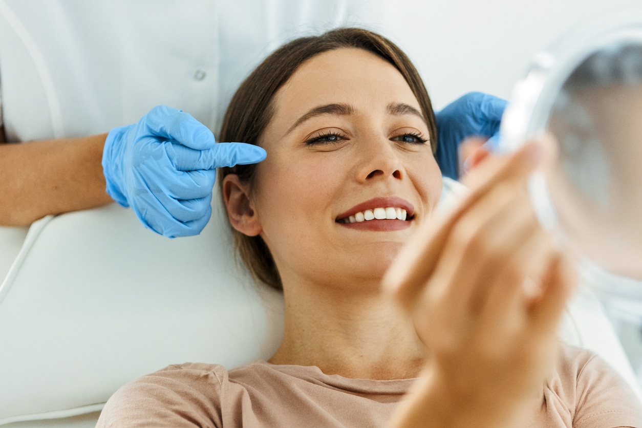 Young woman in her 20s looking in a mirror while a provider assesses crow’s feet before preventive BOTOX® treatment.